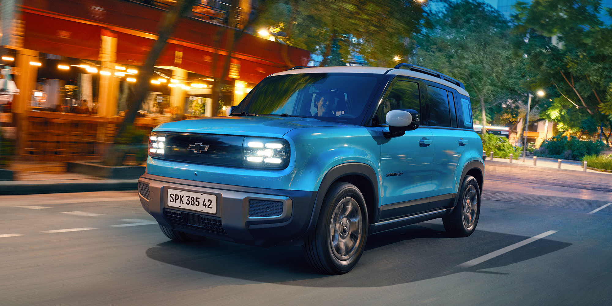 Chevrolet Spark EV color azul circulando por una calle urbana con luz de fondo